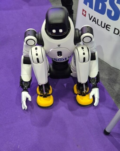 Ein humanoider Roboter kniet auf einem lila Teppich, mit weißen Armen und gelben Füßen.