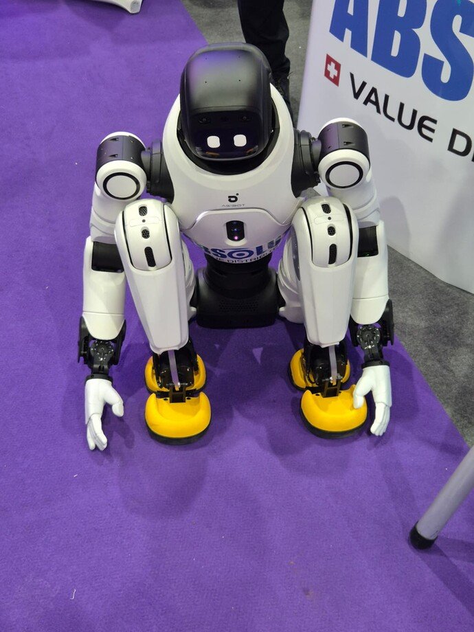 Ein humanoider Roboter kniet auf einem lila Teppich, mit weißen Armen und gelben Füßen.