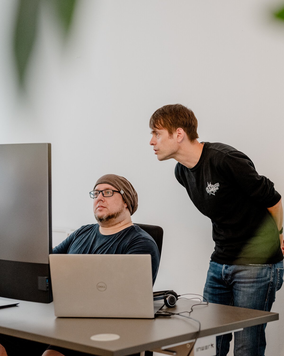 **Bildbeschreibung: IT-Experten bei der Zusammenarbeit im Büro**

In einem modernen IT-Büro diskutieren zwei Experten konzentriert über die neuesten technologischen Trends. Ein Entwickler sitzt vor mehreren Bildschirmen, während ein anderer Kollege neben 