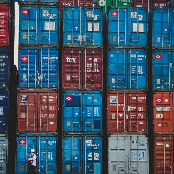 Stapel von farbigen Frachtcontainern auf einem Terminal; Arbeiter mit Helm im Vordergrund.