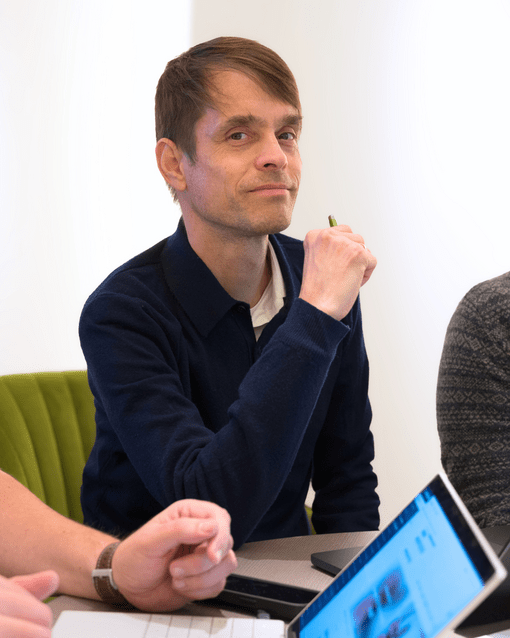 Eine Person sitzt am Tisch und hält einen Stift. Vor ihr liegt ein Tablet.