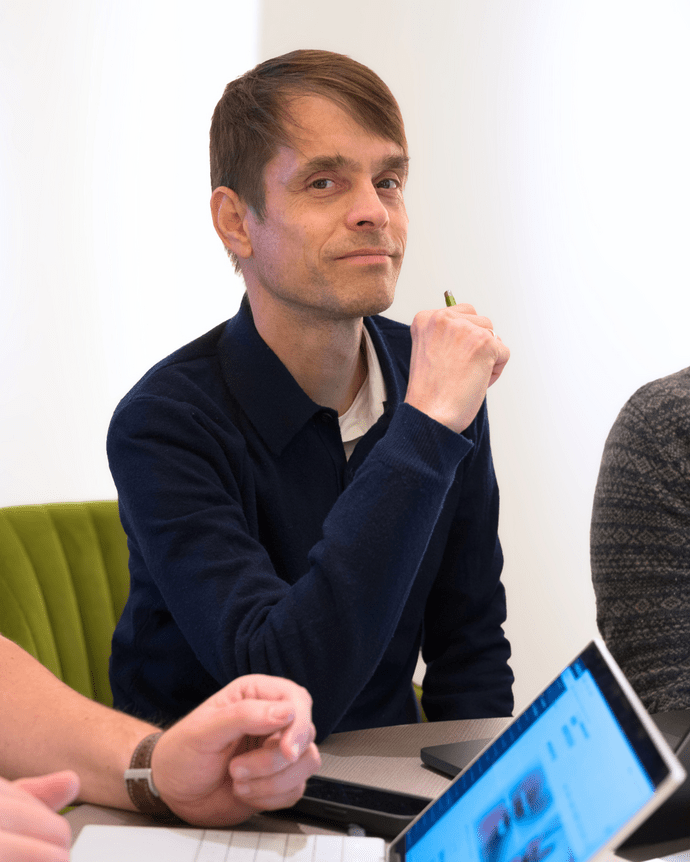 Eine Person sitzt am Tisch und hält einen Stift. Vor ihr liegt ein Tablet.