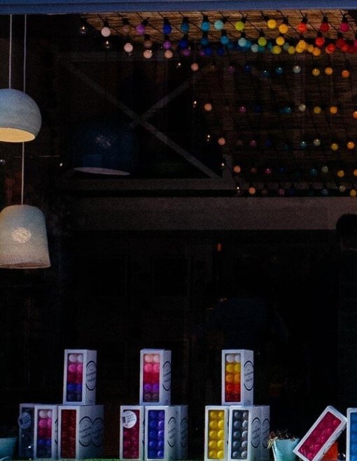 Fahrrad vor einem beleuchteten Lampengeschäft mit großen Fenstern und bunter Lampenvielfalt in einem urbanen Umfeld.