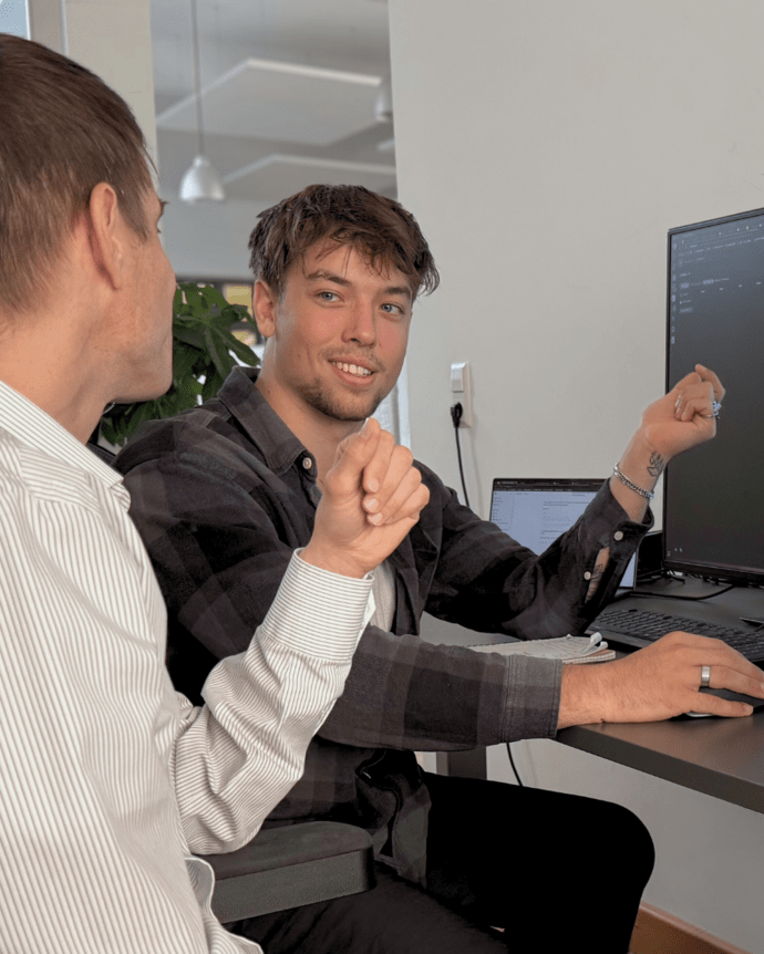 Zwei Männer diskutieren vor einem Computerbildschirm in einem Büro über den dort angezeigten Code.