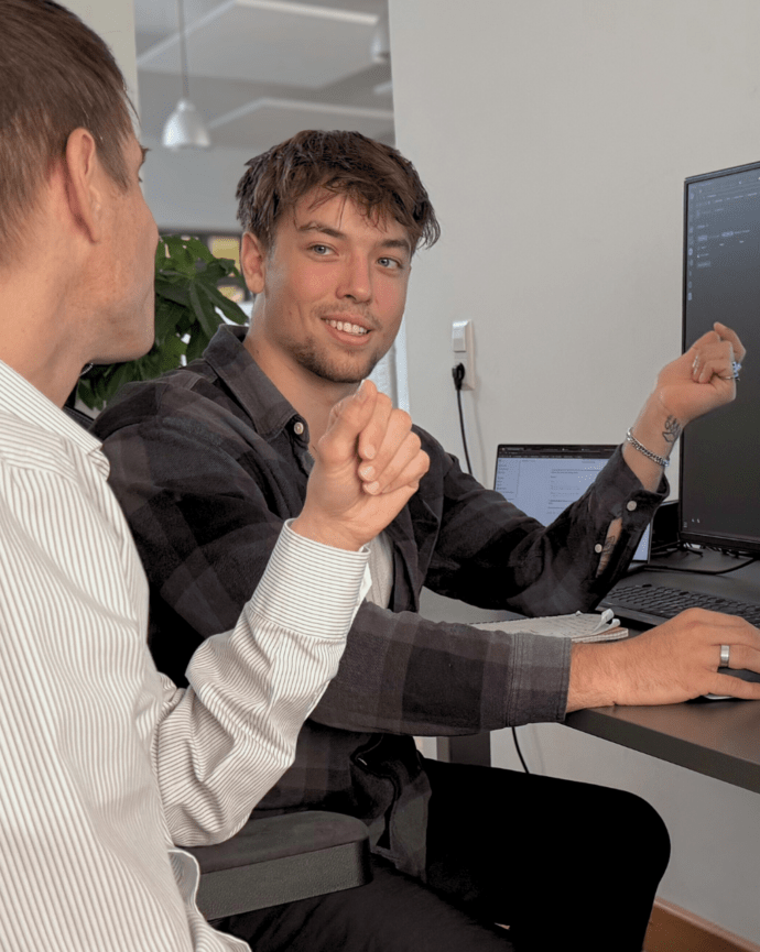 Zwei Männer diskutieren vor einem Computerbildschirm in einem Büro über den dort angezeigten Code.