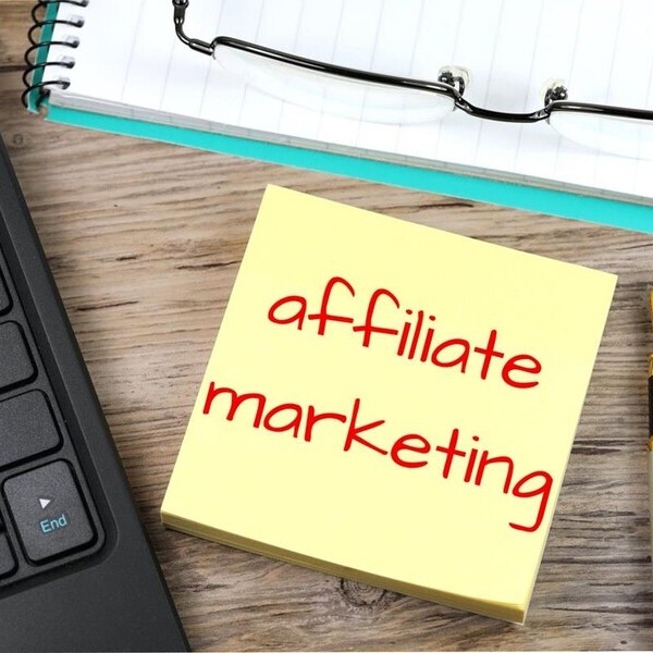 Notiz mit "affiliate marketing" neben Laptop, Stift und Brille auf Schreibtisch.