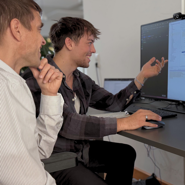 Zwei Männer arbeiten gemeinsam an einem Computerbildschirm in einem Büro und diskutieren vermutlich technische Details.