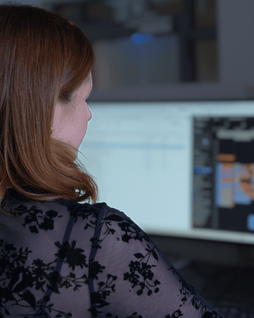 Frau arbeitet an Computerbildschirm mit Diagramm oder Flussdiagramm, trägt schwarze Spitzenbluse.