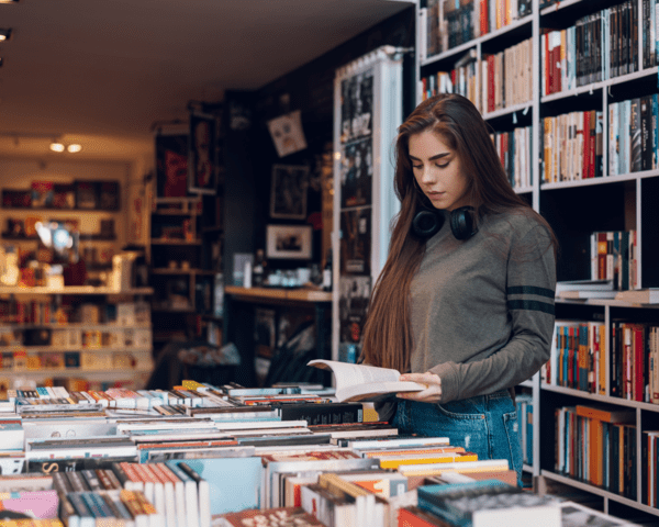 Frau liest ein Buch in einer Buchhandlung, umgeben von Bücherregalen und Tischen voller Bücher.