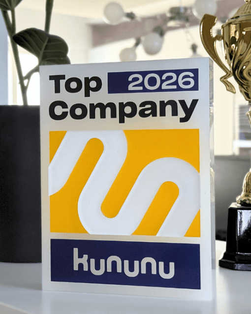 Kununu-Auszeichnung "Top Company 2026", umgeben von einer Pflanze und einem Pokal, auf einem weißen Regal.