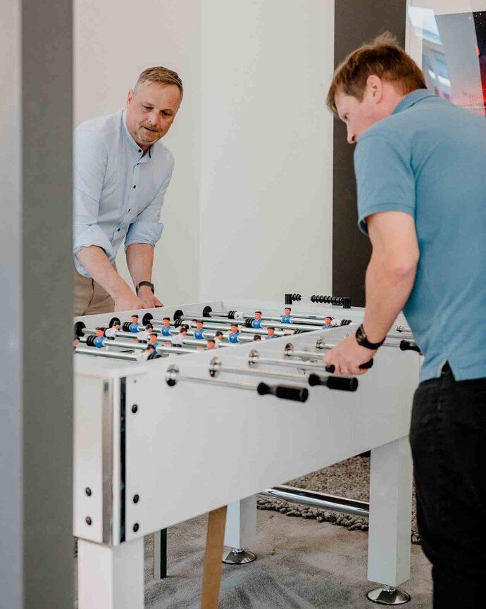 Zwei Männer spielen Tischfußball in einem modernen Büroambiente.