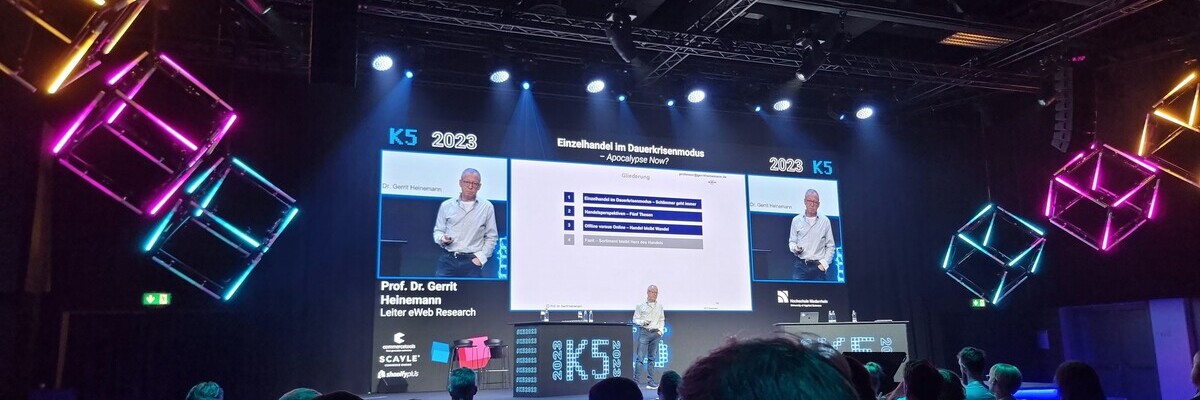 Konferenzbühne mit Vortragendem, Publikum und Präsentationsfolien zum Thema "Einschätzung im Investitionsumfeld" bei der K5 2023.