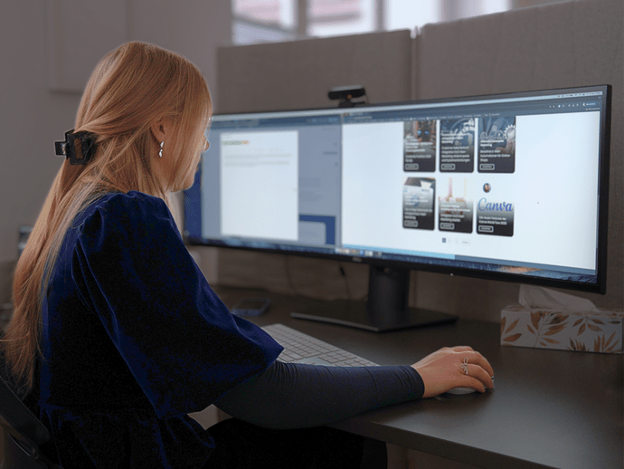 Frau arbeitet an einem breiten Computerbildschirm, der Grafiken und Text zeigt, an einem modernen Schreibtischarbeitsplatz.