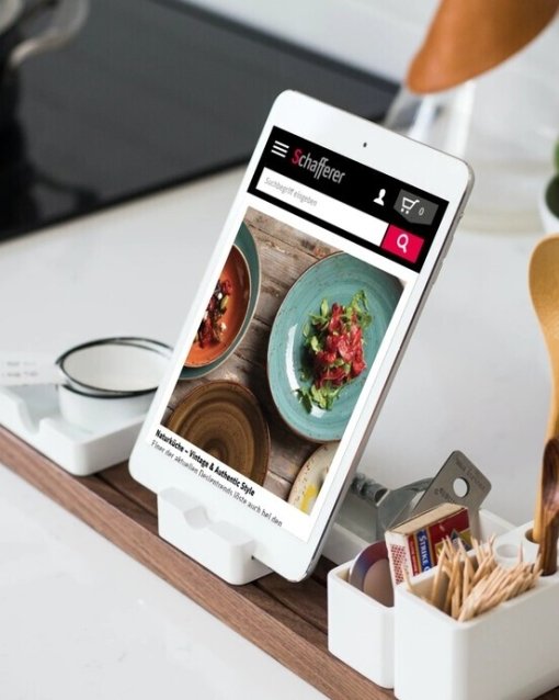 Tablethalter mit Rezeptanzeige, umgeben von Kochutensilien, auf einer Küchenarbeitsfläche.