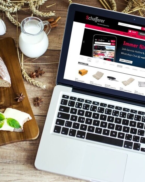 Laptop auf Holztisch mit Brot, Butter und Milch; Website auf dem Bildschirm.