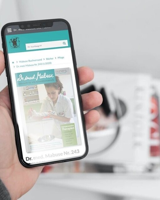 Smartphone in Hand mit aufgerufenem Magazin "Dr. med. Mabuse", im Hintergrund unscharfe Zeitschriften auf einem Tisch.