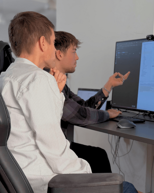 Zwei Männer arbeiten am Computer und besprechen Code auf einem Monitor.