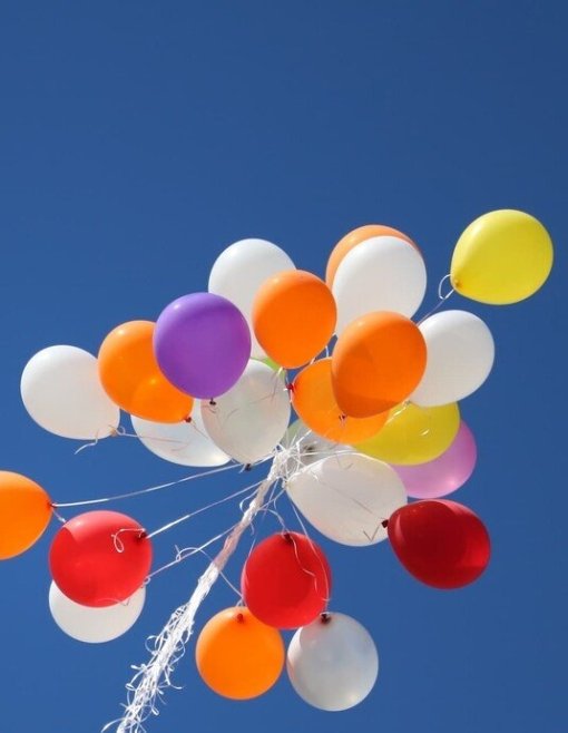 Bunte Luftballons schweben vor wolkenlosem Himmel.