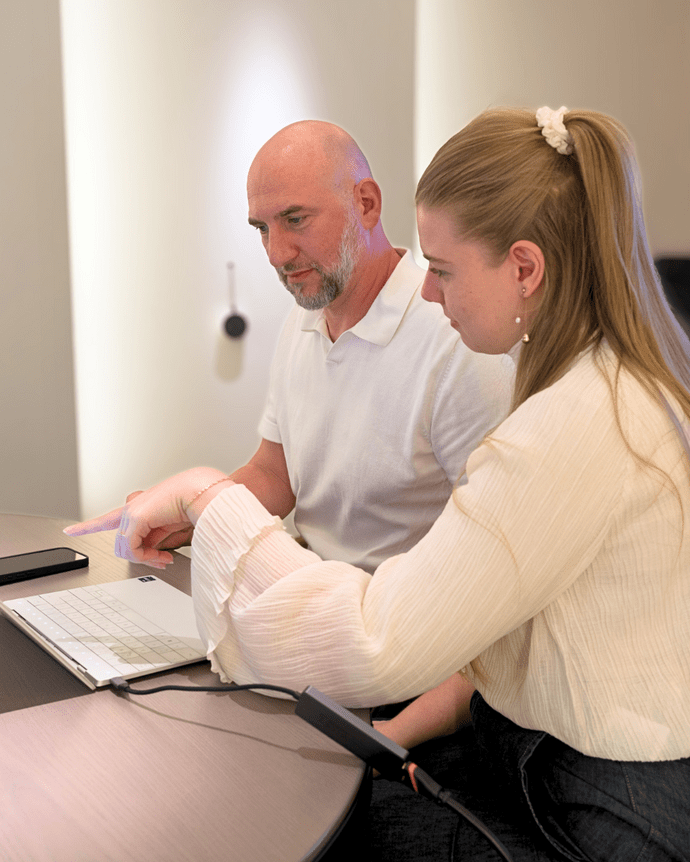 Zwei Personen arbeiten konzentriert an einem Laptop in einem modernen Büroraum.