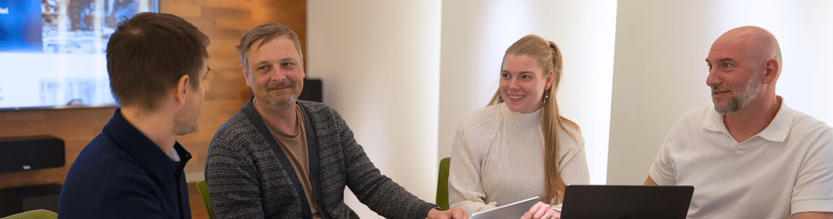 Personengruppe in einem modernen Besprechungsraum mit Laptops und Notizen, engagiert in einer Diskussion.