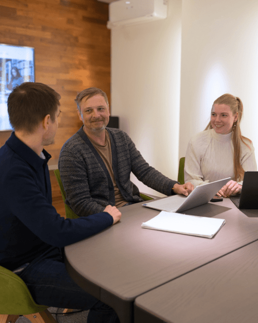 Personengruppe in einem modernen Besprechungsraum mit Laptops und Notizen, engagiert in einer Diskussion.