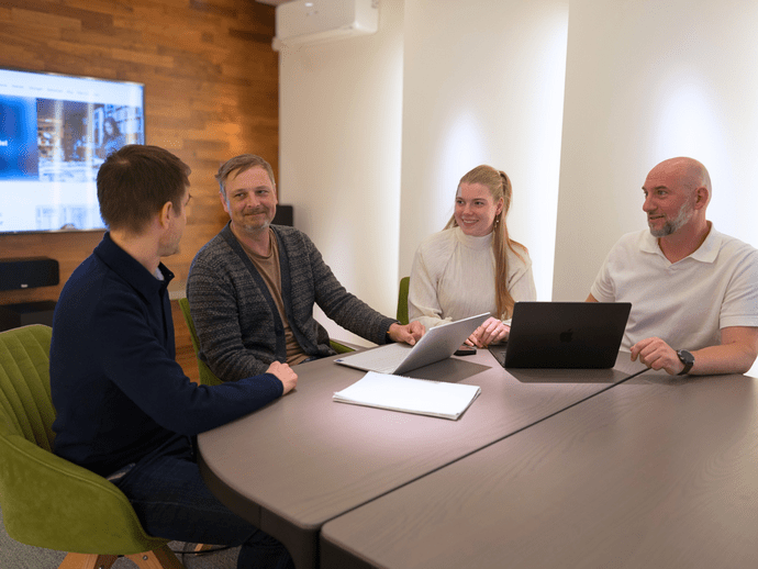 Personengruppe in einem modernen Besprechungsraum mit Laptops und Notizen, engagiert in einer Diskussion.