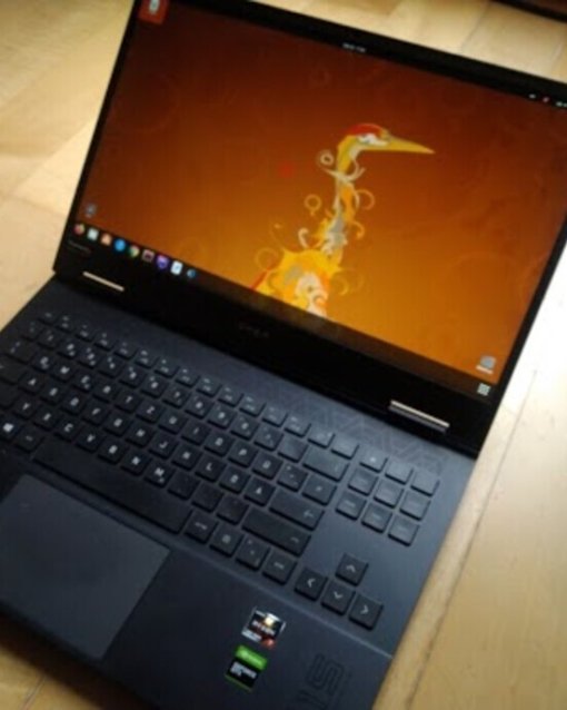 Laptop auf Holzfußboden, geöffneter Bildschirm mit orangefarbenem Hintergrund und abstraktem Design, Tastatur sichtbar.