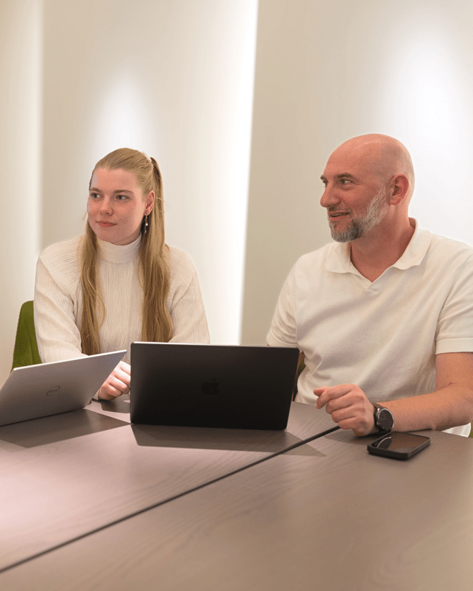 Vier Personen diskutieren an einem ovalen Tisch mit Laptops in einem modern beleuchteten Besprechungsraum.