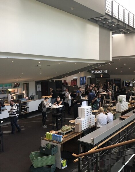 Menschen&#x20;versammeln&#x20;sich&#x20;in&#x20;einem&#x20;modernen,&#x20;offenen&#x20;Raum&#x20;mit&#x20;Cafeteria&#x20;und&#x20;mehreren&#x20;Sitzbereichen,&#x20;beleuchtet&#x20;durch&#x20;Oberlichter.