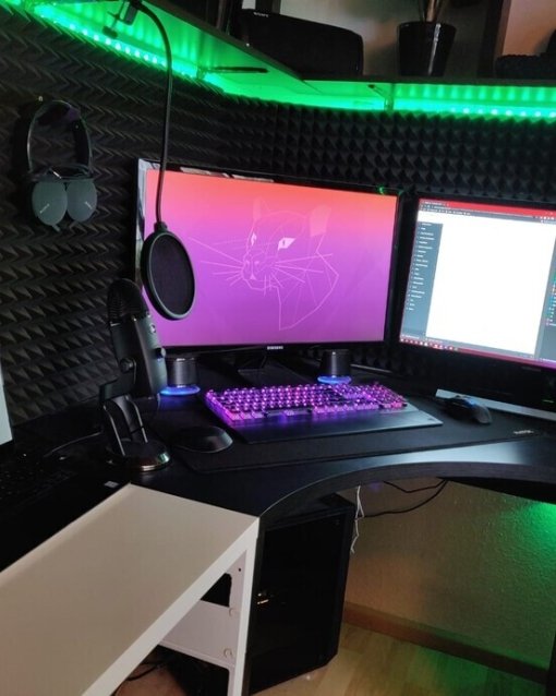 Moderne Gaming- und Arbeitsstation mit zwei Monitoren, Laptop, RGB-Tastatur und Tonaufnahme-Equipment, umgeben von Schallschutzmatten.