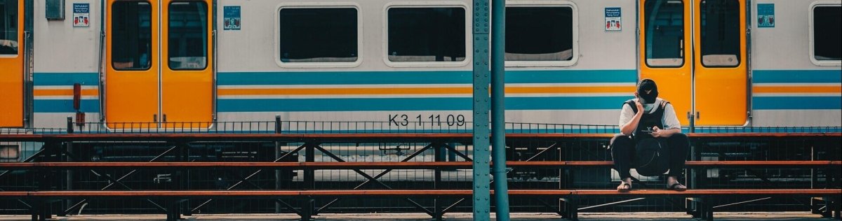 Person sitzt auf Bahnhofsbänken vor gelbem Zug, vertieft in ein Buch, unter überdachtem Bahnsteig.