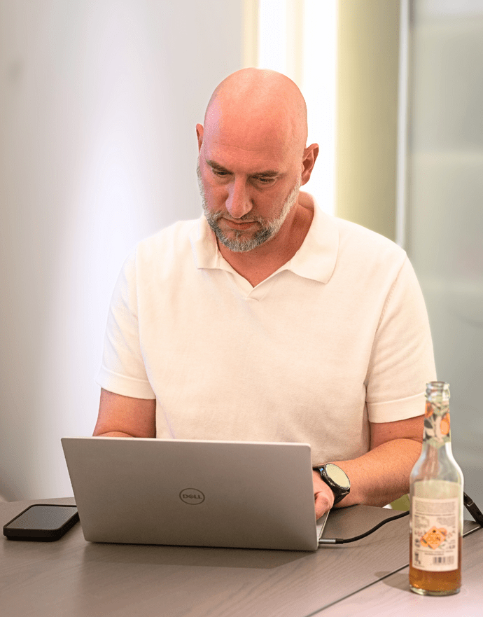 Ein Mann arbeitet in einem modernen Büro an einem Laptop, neben ihm steht eine geöffnete Flasche Getränk auf dem Tisch.