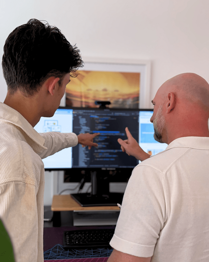 Zwei Männer diskutieren und zeigen auf Code auf einem Computerbildschirm in einem Büro.