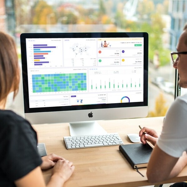 Zwei Personen analysieren Datenvisualisierungen auf einem Computerbildschirm in einem modernen Büro.