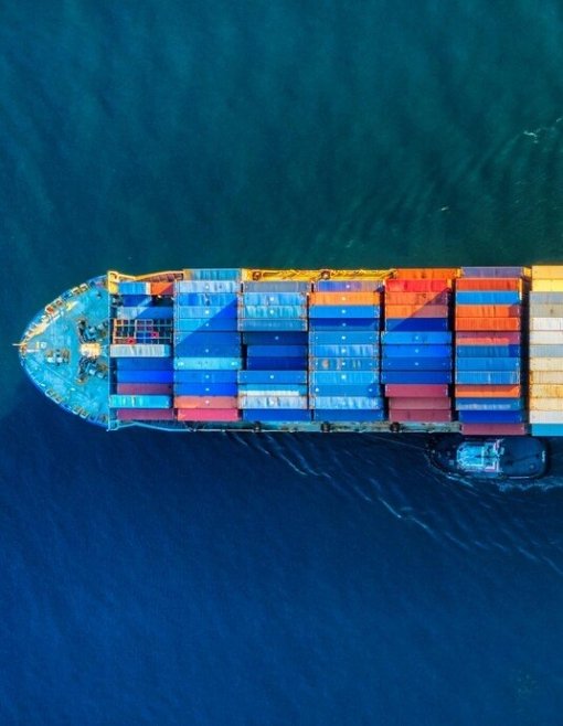 Luftaufnahme eines fahrenden Containerschiffs mit bunten Frachtcontainern im Meer.