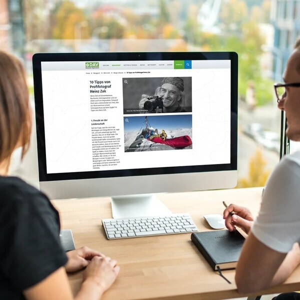 Zwei Personen betrachten einen Computerbildschirm mit einem Artikel über Fotografie in einem modernen Büro mit Stadtblick.