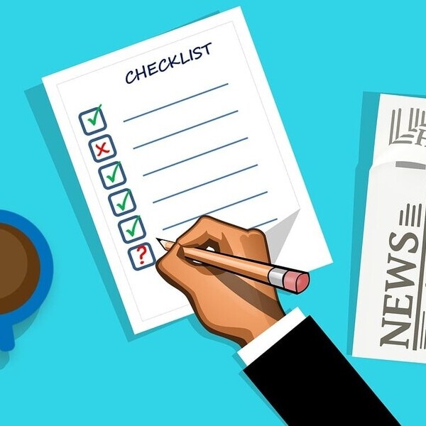 Eine Hand markiert eine Checkliste, neben einer Kaffeetasse und einer Zeitung auf einem blauen Hintergrund.