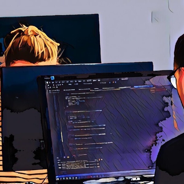 Zwei Personen arbeiten an Computern, einer zeigt Code auf dem Bildschirm.