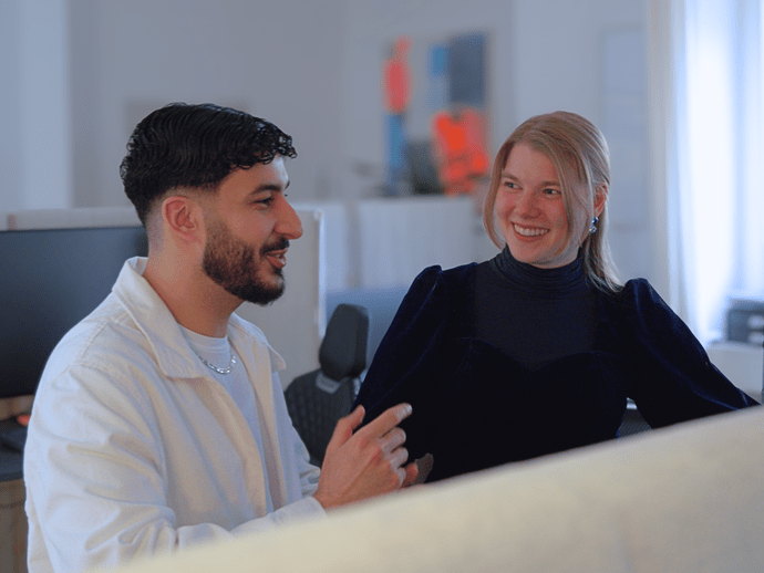 Zwei Personen unterhalten sich in einem Büro, umgeben von modernen Arbeitsplätzen und technischer Ausstattung.