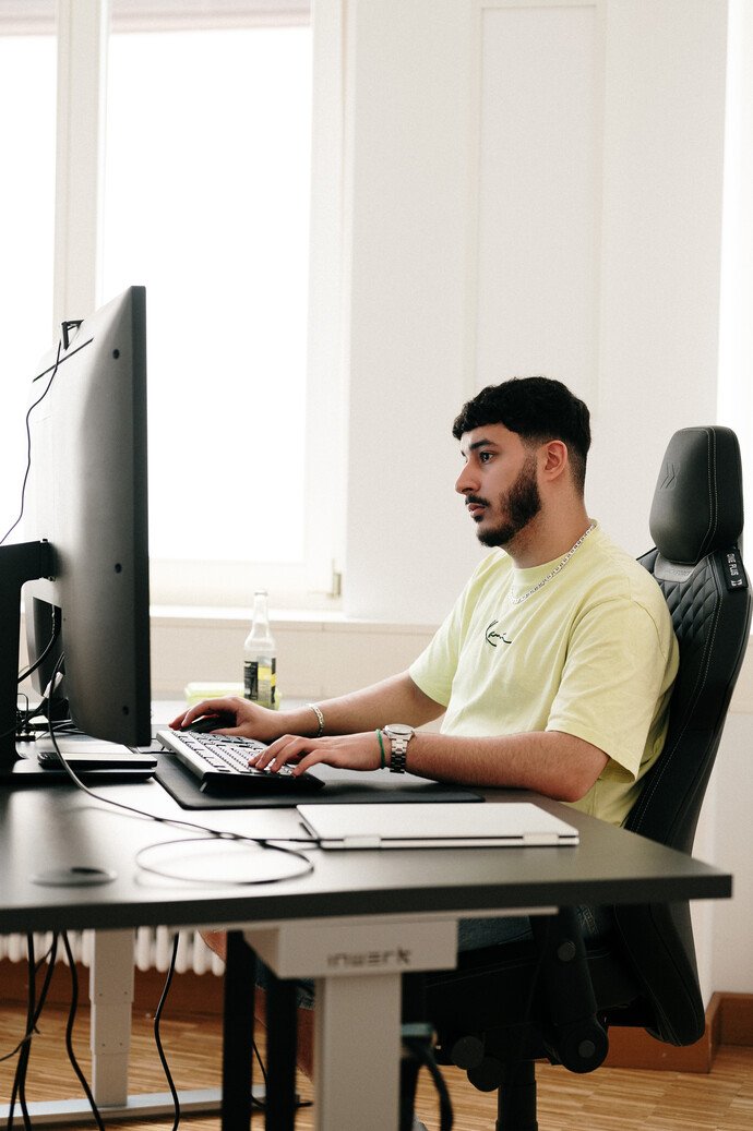 Person am Schreibtisch arbeitet konzentriert am Computer, ein Getränk steht daneben.