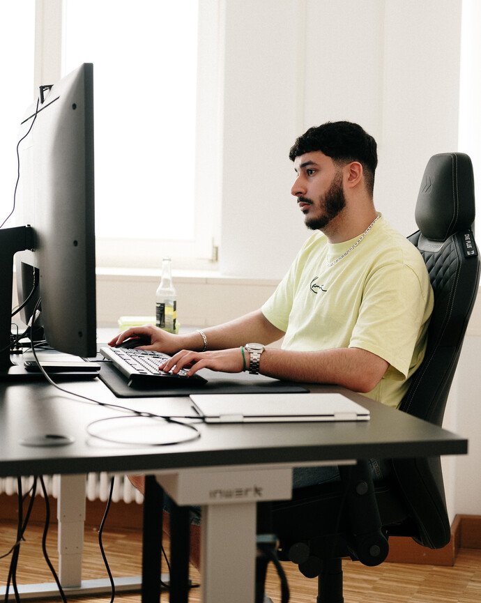 Person am Schreibtisch arbeitet konzentriert am Computer, ein Getränk steht daneben.