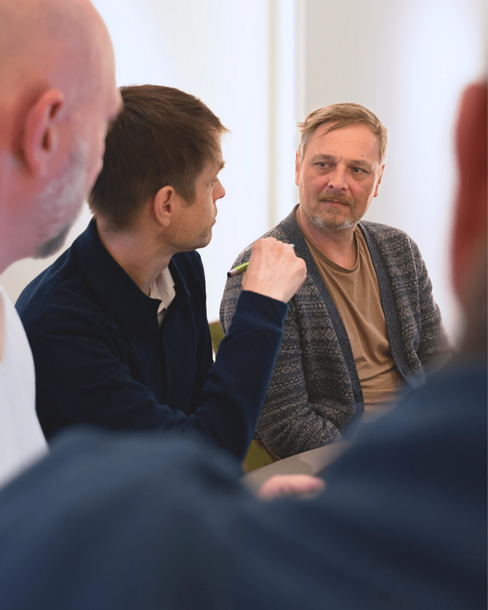 Vier Männer in Diskussion in einem Konferenzraum, fokussiert auf zwei Männer, die sich intensiv unterhalten.