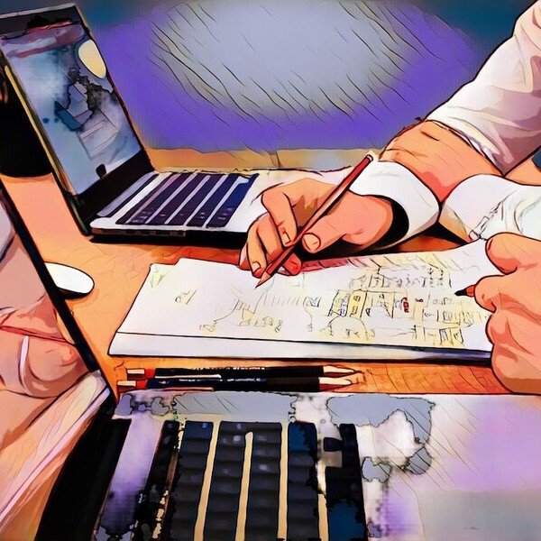 Person arbeitet an einem Schreibtisch mit Laptops und Papieren, macht Notizen mit Bleistiften in kreativer Umgebung.