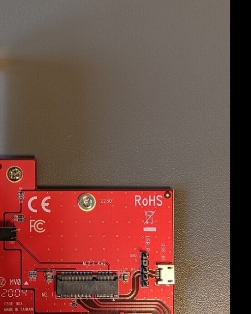 Rote PCIe-Adapterkarte mit Schrauben, Steckplatz und gekennzeichneten Komponenten auf grauem Hintergrund.