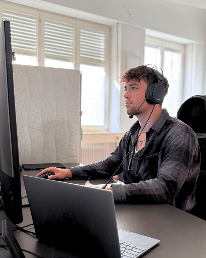 Mann mit Kopfhörern arbeitet konzentriert an Computerbildschirmen in einem Büro.