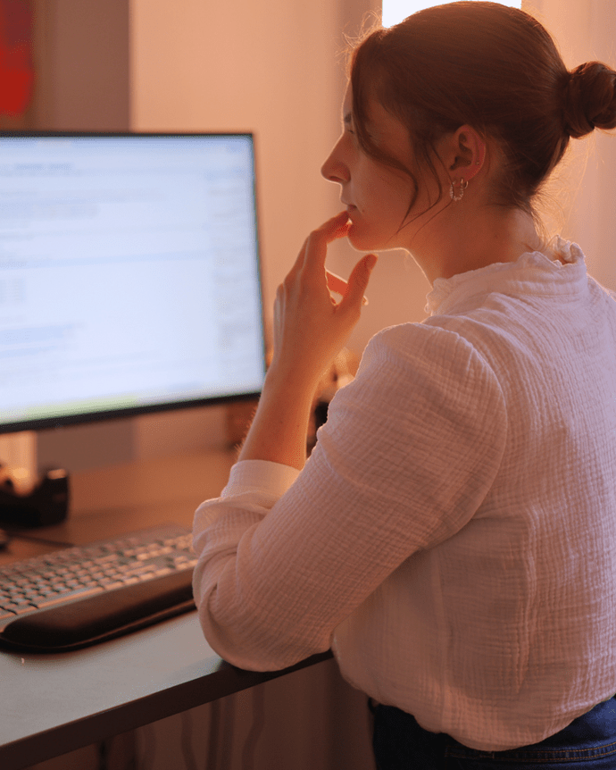 Eine Frau arbeitet nachdenklich an einem Computer mit großem Bildschirm in einem Büro.