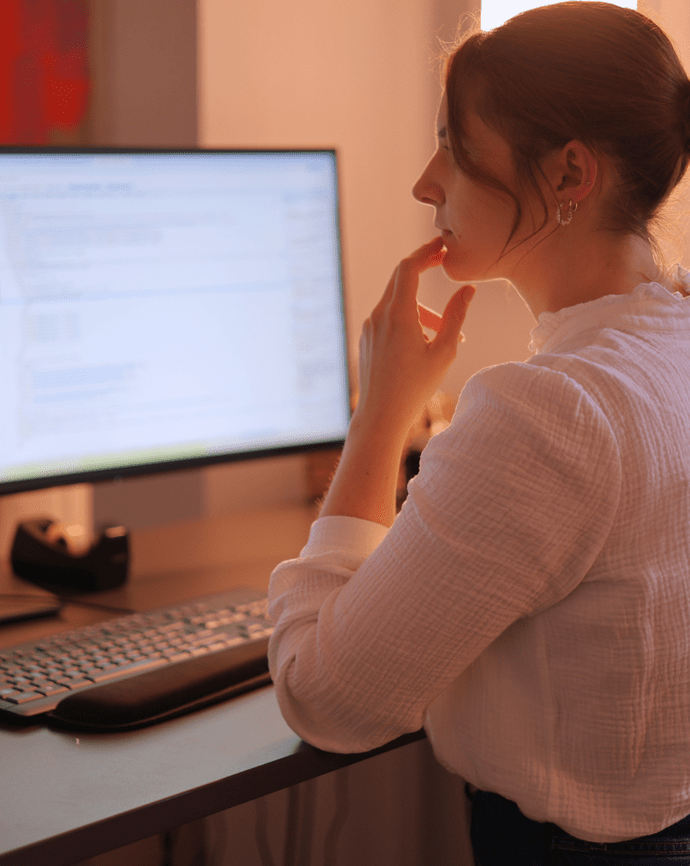 Eine Frau arbeitet nachdenklich an einem Computer mit großem Bildschirm in einem Büro.