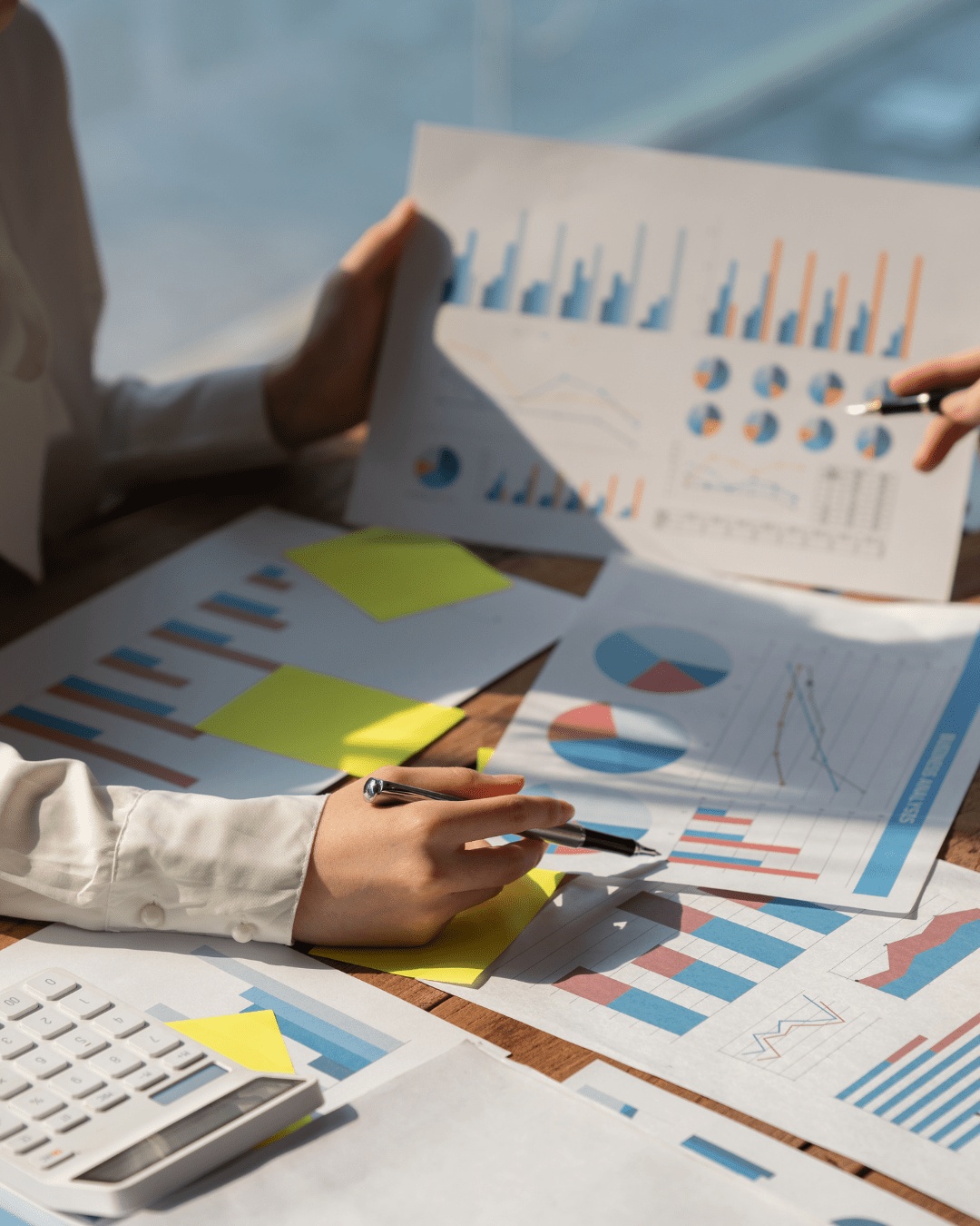 Personen analysieren Finanzdiagramme auf Schreibtisch. Tabellen, Diagramme und ein Taschenrechner sind sichtbar.