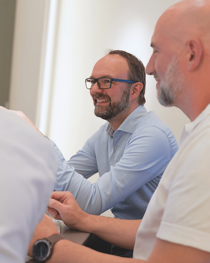 Zwei Männer in einem Meeting lächeln und diskutieren, während sie an einem Tisch sitzen.