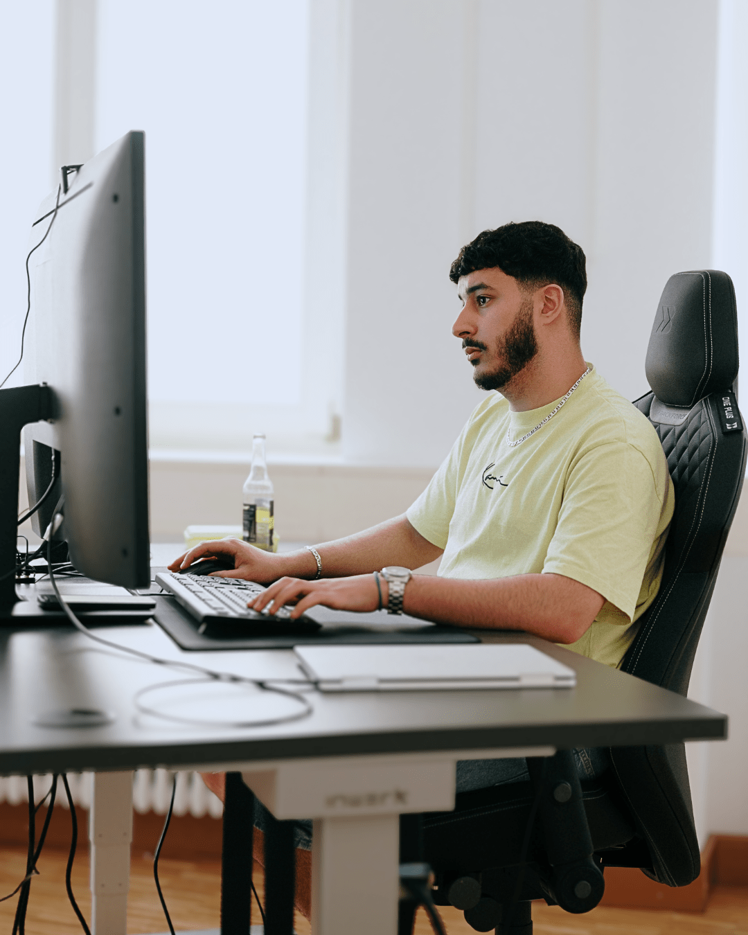 Mann am Computerarbeitsplatz mit Getränk in modernem Büro, vertieft in die Arbeit.